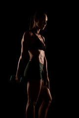 Fototapeta premium Side Profile of a Fit Woman Holding Dumbbells on a Dark Background