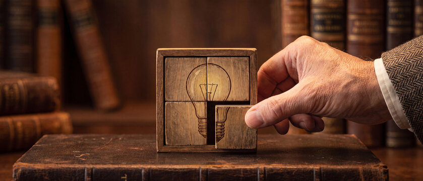 Mans hand solving a wooden puzzle with a lightbulb design, representing ideas, creativity, and problemsolving, set against a backdrop of classic books in a library