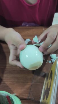 
A toddler's hands are peeling a hard-boiled egg on the table.