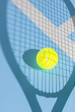 blue background with yellow tennis ball and shadow of a tennis racket
