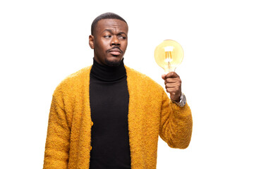 Young man in a cozy sweater holds a vintage light bulb, symbolizing creativity and innovation. He stands against a bright background, deep in thought, reflecting on new ideas and inspiration. © Nikola Spasenoski