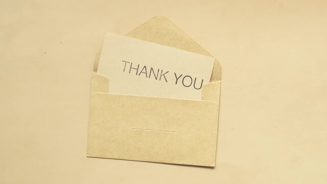 Stop motion animation of kraft envelope with thank you card sliding across parchment background