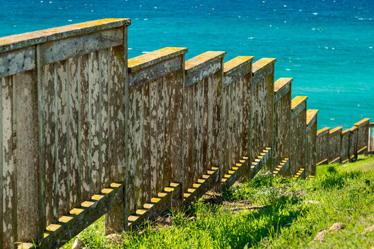 Italy, Sardinia, Oristano.  Weathered wooden fence descending a hill towards the Mediterranean Sea.
