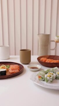 Hands Using Chopsticks to Dip Sushi Piece into Sauce with Assorted Sushi on Table