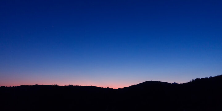 Sunset over silhouetted hilly horizon landscape.