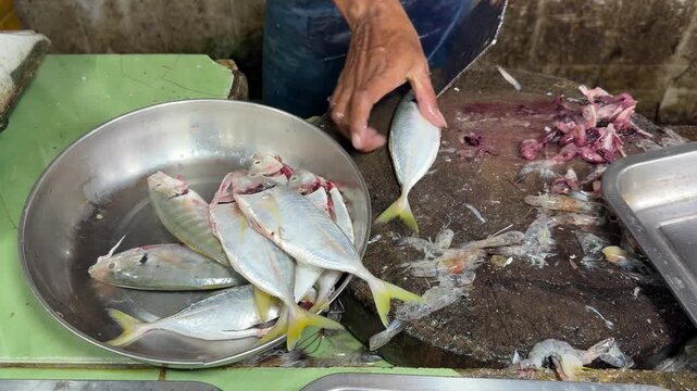 Cutting and cleaning fresh raw fish on a wooden chopping block in a traditional market