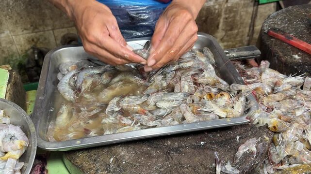 Hand cleaning and peeling raw shrimp in a market stall