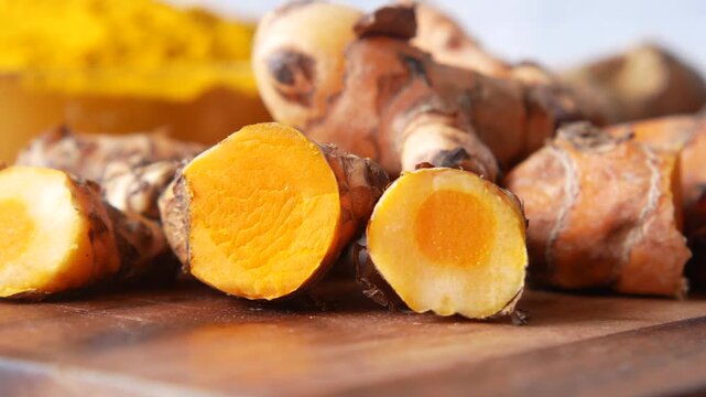 Close up of fresh turmeric roots and powder on cutting board, essential spice for healthy cooking and traditional medicine