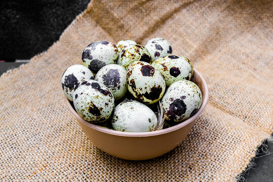 a collection of speckled quail eggs surrounded by soft quail feathers in a brown bowl on burlap
