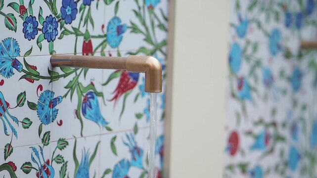 Water flowing from a metal tap against colorful tile wall design