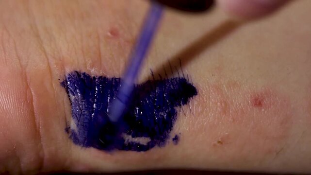 Applying dark blue mascara to a person's skin for testing