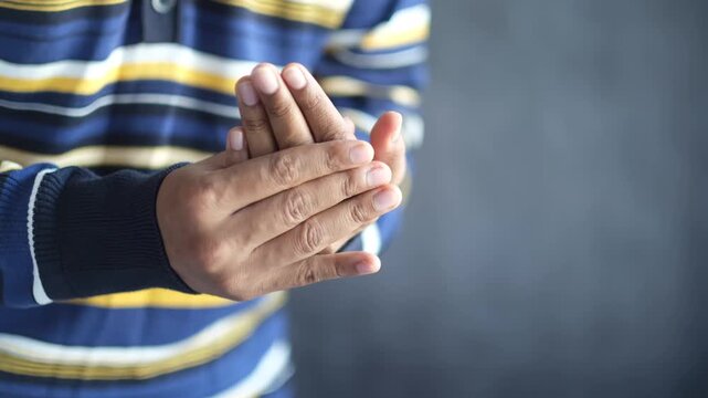 A man in a striped shirt rubs his hands together, illustrating comfort or a mild sensation, captured in a close-up indoor shot.