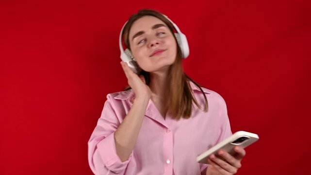  woman enjoys listening to music in studio on red background. 