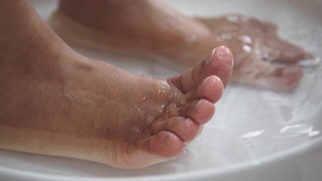 Woman soaking feet in warm water for spa treatment and relaxation in white basin