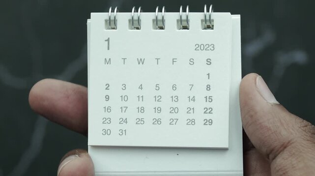 Close-up of a person holding a white desk calendar showing January 2023