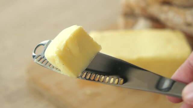 Close up of butter being cut on a knife with a textured edge, fresh butter block in background