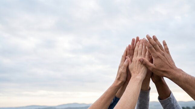 Diverse Group of People Joining Hands Together for Teamwork and Unity Against Cloudy Sky
