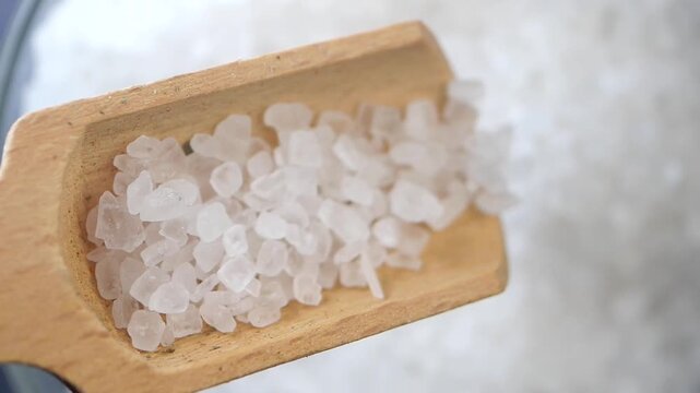 Close up video of rock salt falling from a wooden spoon, slow motion footage of salt crystal pouring into a white bowl