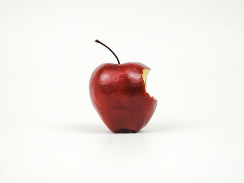 Fresh red apple with a single visible bite mark taken out of the left side, featuring a dark stem and isolated on a clean white background.