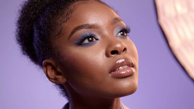 Young woman with glittery blue eyeshadow and glossy lips posing against a soft purple studio background