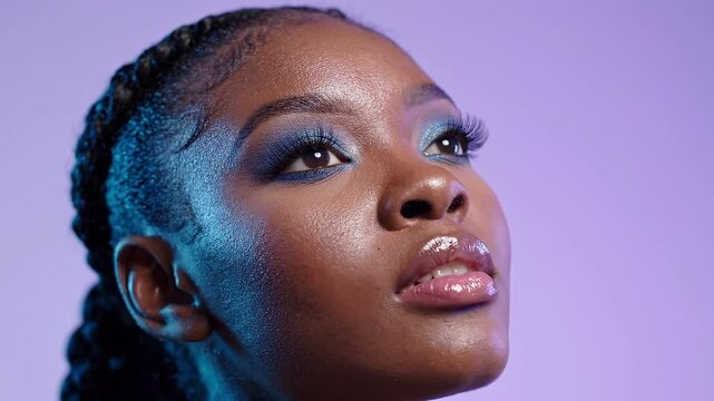 Young woman with shimmering blue eyeshadow posing against solid purple background in studio lighting setup