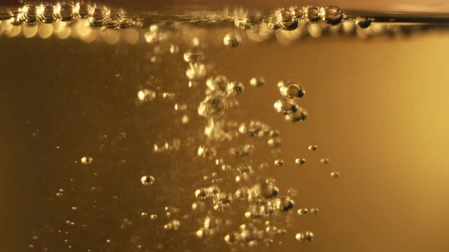Close-up shot of rising sparkling bubbles in a golden fizzy drink creating a refreshing visual texture