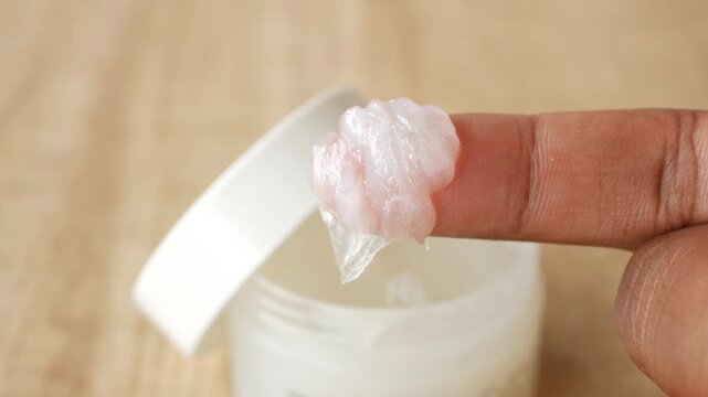 Close up finger scooping petroleum jelly from a jar for skin care and beauty treatments