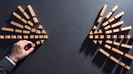 Fototapeta premium Businessman hand arranging small wooden blocks into arrow shapes on dark stone surface for strategic business planning, leadership development, direction, and growth vision concept.
