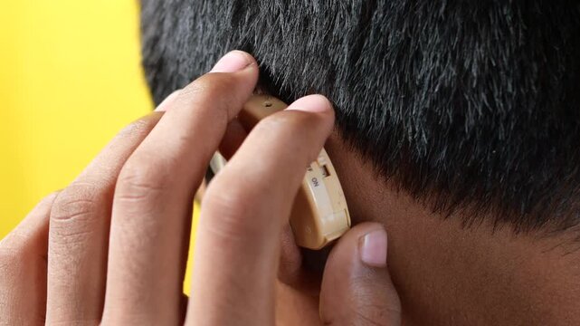 Hearing aid device behind ear of young man for auditory support and sound amplification