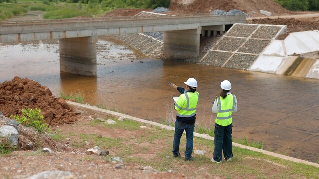 Civil Engineers in Neon Vests Pointing and Inspecting Concrete Bridge and Riprap Slope Canal Infrastructure 4K