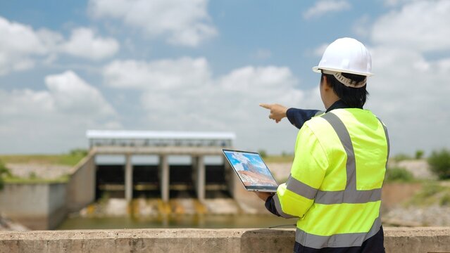 Hydraulic Engineer with Laptop Pointing at Concrete Water Sluice Gate Dam During Infrastructure Field Inspection 4K