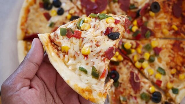 Close up of hand holding delicious pizza slice with colorful toppings