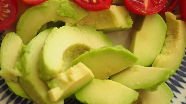Close up top shot of fresh avocado and cherry tomato slices on a white and blue patterned plate for a healthy meal motion footage