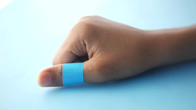 Person showing thumb wrapped in blue adhesive bandage on light background