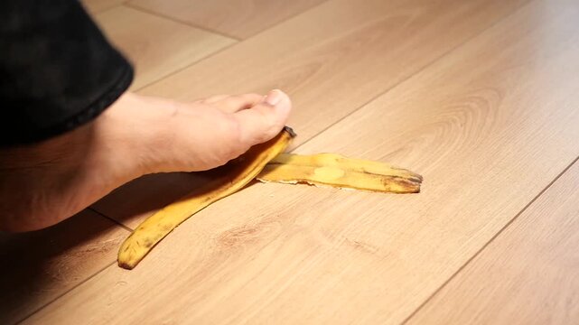 Bare foot stepping on banana peel on wooden floor indoors with slip hazard and danger concept