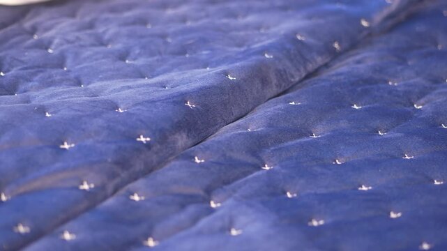 Cinematic close up of blue velvet quilted bedspread with silver decorative embroidery stitches in bedroom setting