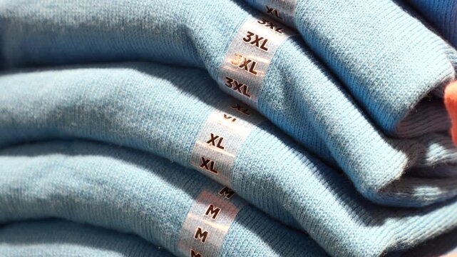 Close-up shot of neatly folded blue shirts with various size labels including M, XL, and 3XL on display in retail store