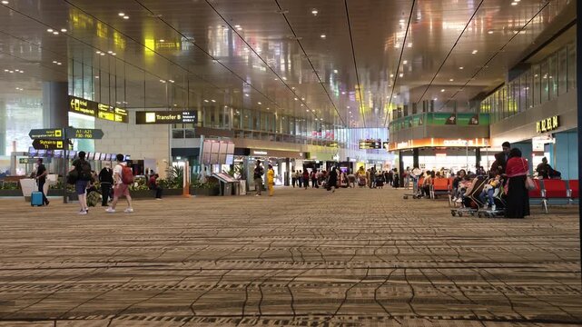 Busy airport terminal concourse with travelers moving through with luggage and shopping areas.
