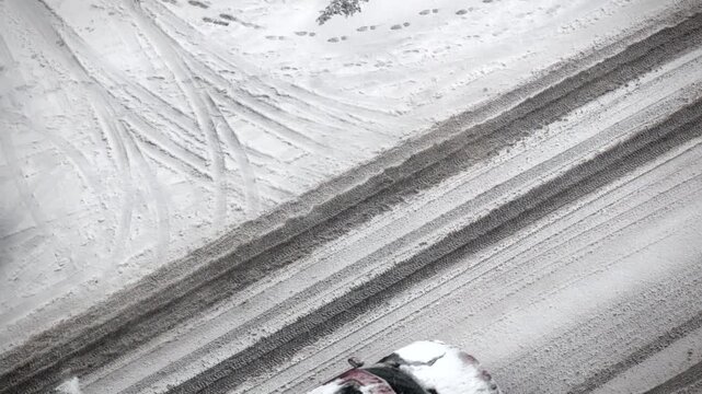 Aerial view of snowy road with car driving through winter slush and tire tracks on white pavement in high angle shot