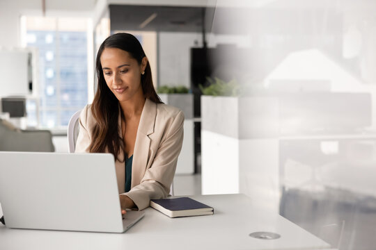 Businesswoman sits at office desk, working on project or corporate digital tasks, typing on laptop, responding on business emails, consulting clients or browsing. Administrative workflow management