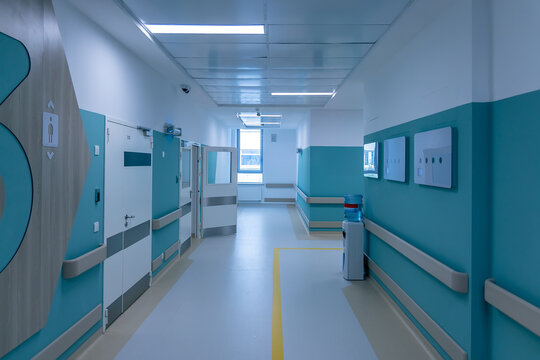 A quiet hospital corridor with turquoise walls and closed ward doors. Handrails run along the walls to support patients who walk on their own. Interior of a new and modern hospital