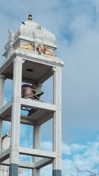 White ornamental bell tower with golden Hindu sculptures at Munneswaram Temple in Chilaw, Sri Lanka, against a bright blue sky.