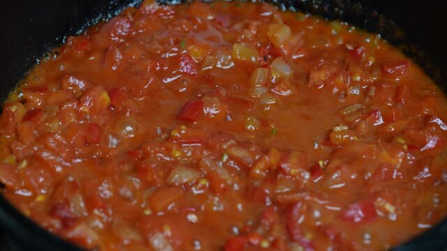 Cooking thick homemade tomato sauce. Close-up of simmering chunky red tomato sauce with onions and peppers cooking in pan, texture background