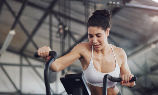 Fitness, girl and gym with exercise bike, cardio workout and burning calories for wellness. Sweating, athlete and intense challenge on stationary bicycle for physical activity, stamina and endurance