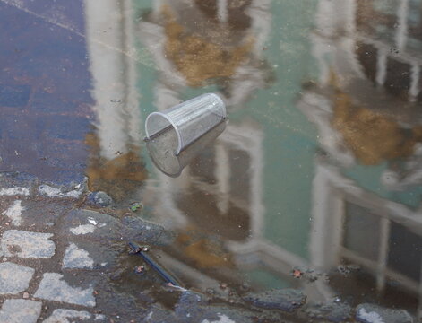 A transparent plastic cup is lying in a puddle on the paving stones