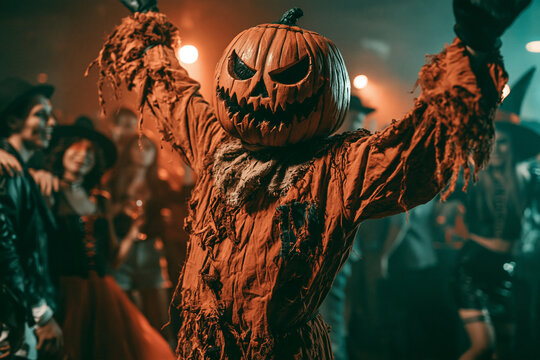 Pumpkin-Head Scarecrow at the Halloween Costume Party Raising Arms in a Dark Spooky Celebration with Friends