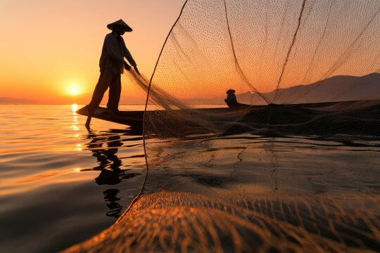 Silhouetted fisherman casts net from boat at sunrise on calm water