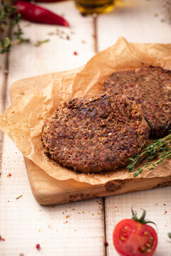 Two succulent fried beef patties for burgers seasoned with herbs presented on parchment paper on rustic wooden board 
