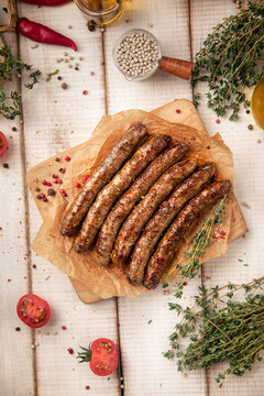 Juicy roasted grilled sausages served on parchment paper on wooden cutting board with herbs and spices