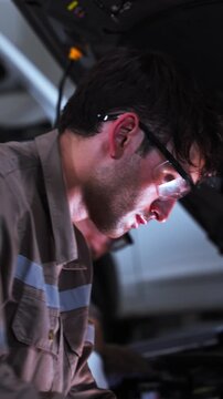 Two experienced automotive technicians work together while inspecting a vehicle engine inside a modern repair garage. The image represents teamwork, collaboration, technical expertise, diagnostics, pr
